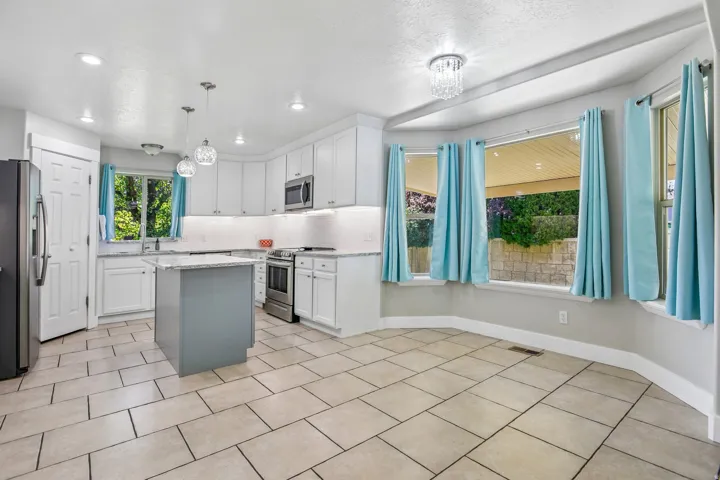 Kitchen and dining area featuring a central island, white cabinetry, stainless steel appliances, and a tiled backsplash