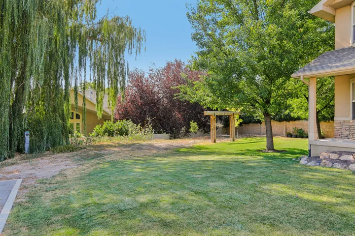 Expansive exterior yard space featuring a manicured lawn, mature trees, and a wooden arbor