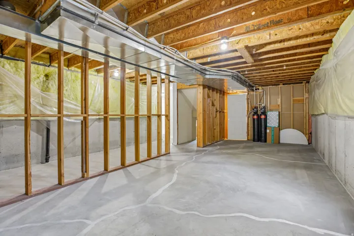 Unfinished basement with concrete flooring, exposed wood framing, ceiling joists, and visible ductwork