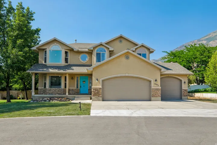 Stucco exterior with stone veneer accents, multi-pane arched windows, a bright blue entry door, and a two-car garage with arched doors