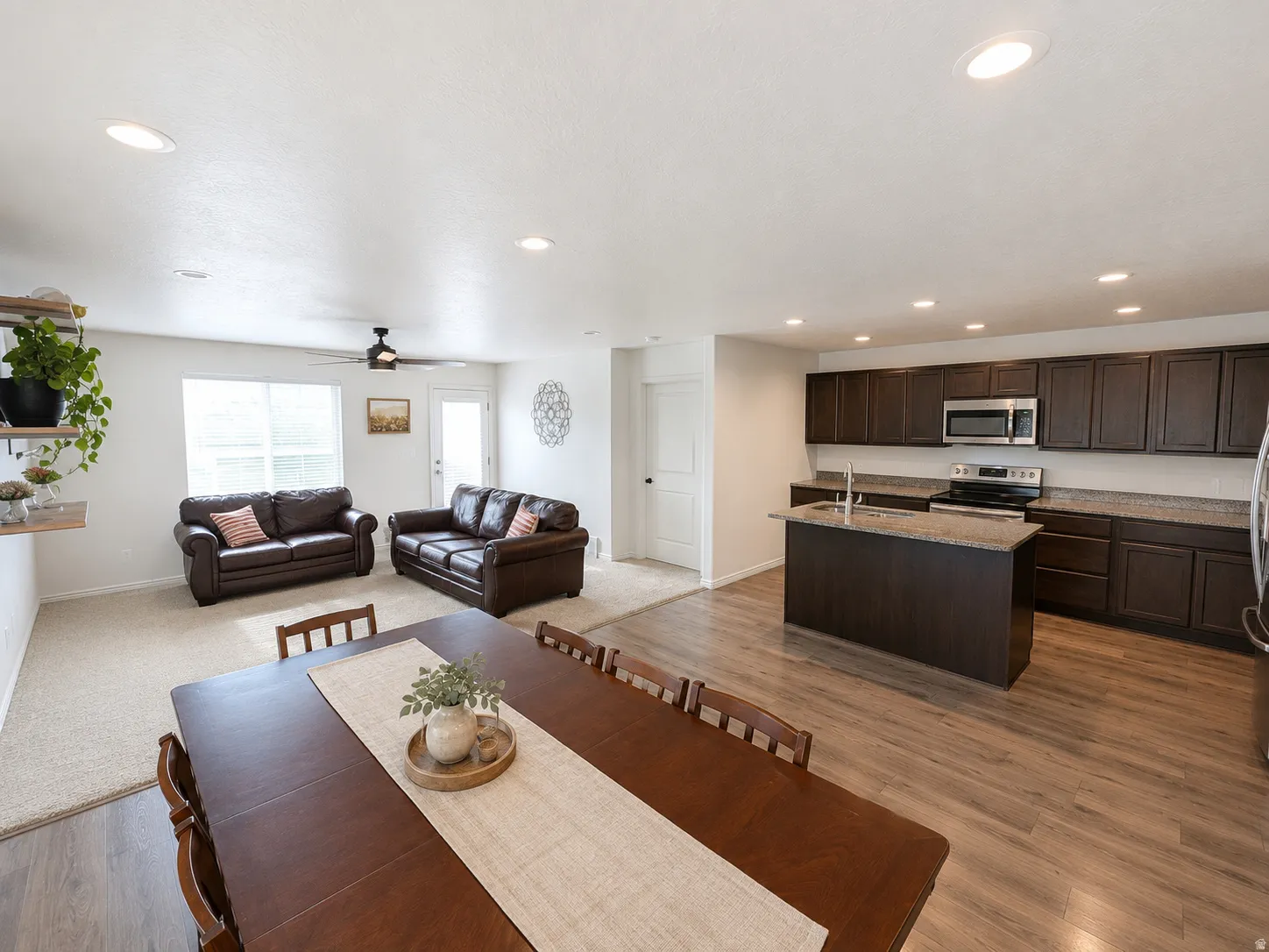 Open concept living area featuring wood-finish flooring in the kitchen, dark wood cabinetry, stainless steel appliances, and recessed lighting