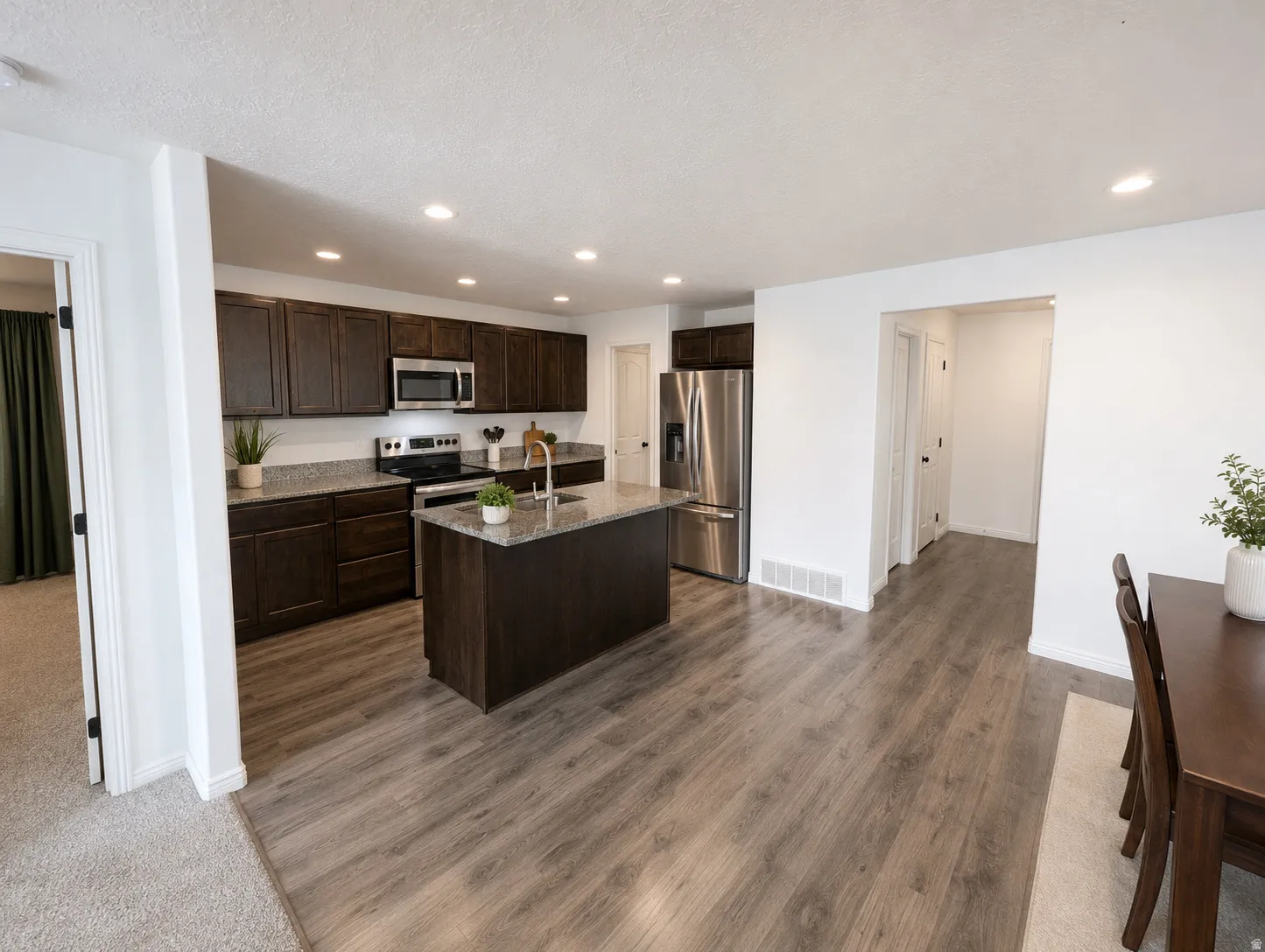Kitchen featuring dark wood cabinetry, stainless steel appliances, a center island with a sink, stone countertops, and wood-finish flooring