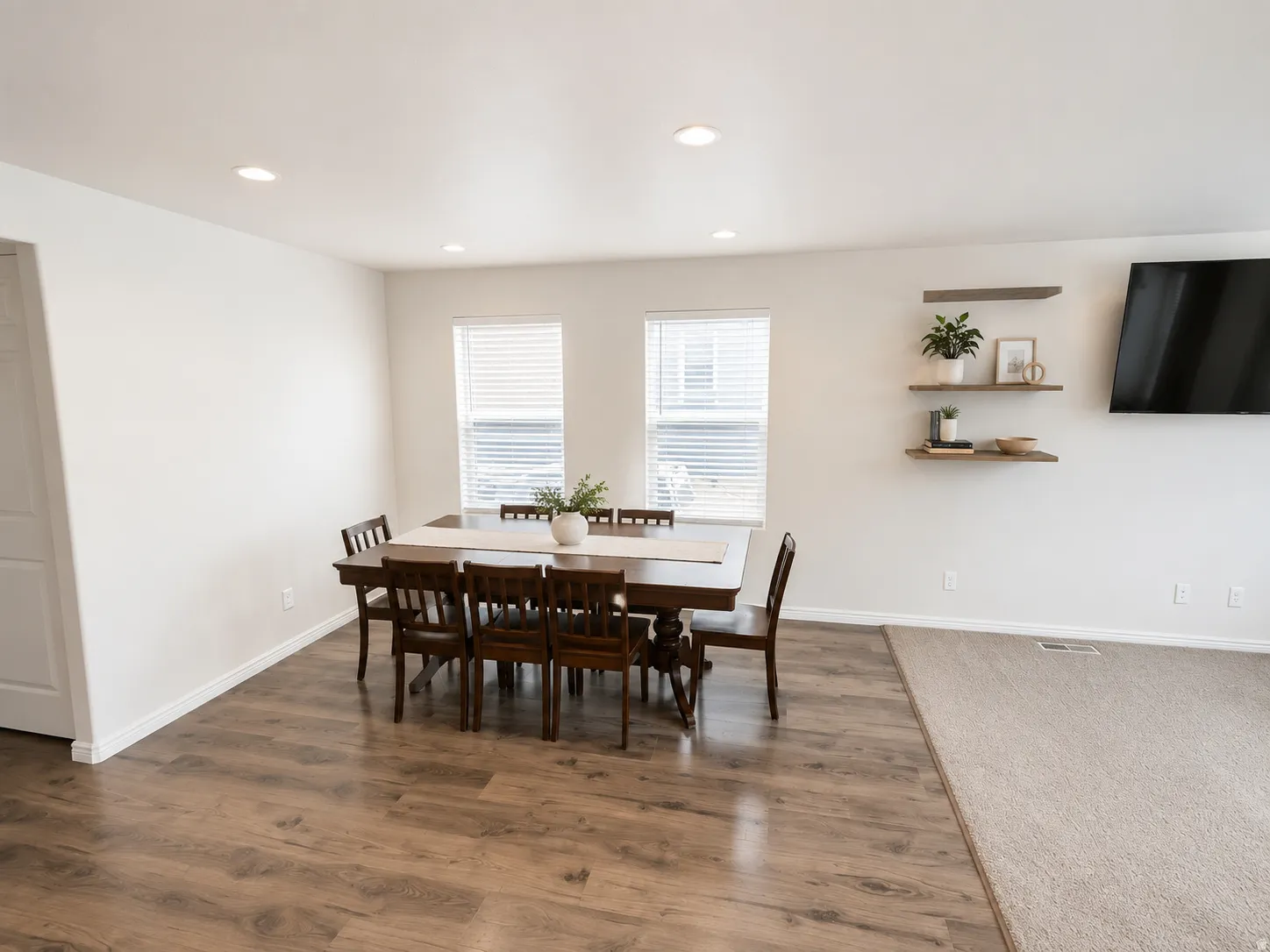 Open-concept dining and living area featuring wood-finish flooring, recessed ceiling lighting, and large dual windows with plantation shutters