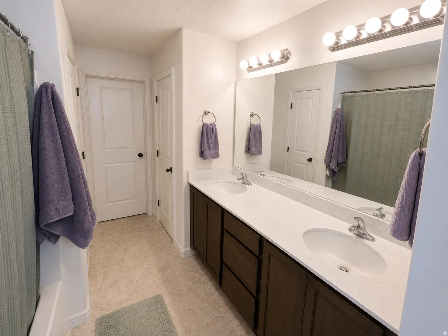 Dual-sink bathroom vanity featuring white quartz countertops, dark wood cabinetry with ample storage, and chrome fixtures