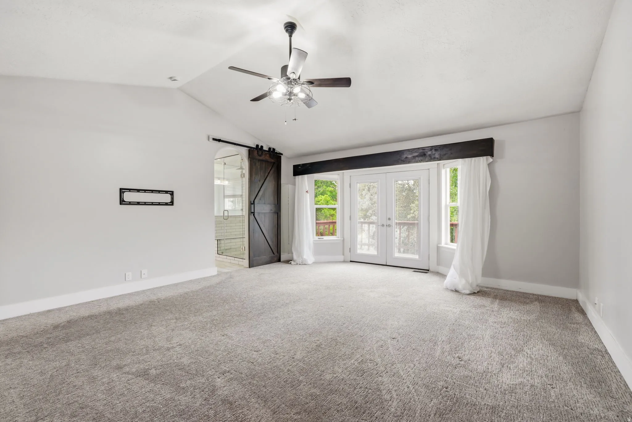 Spacious interior featuring a vaulted ceiling with a ceiling fan, plush grey carpeting, and light grey wall finishes