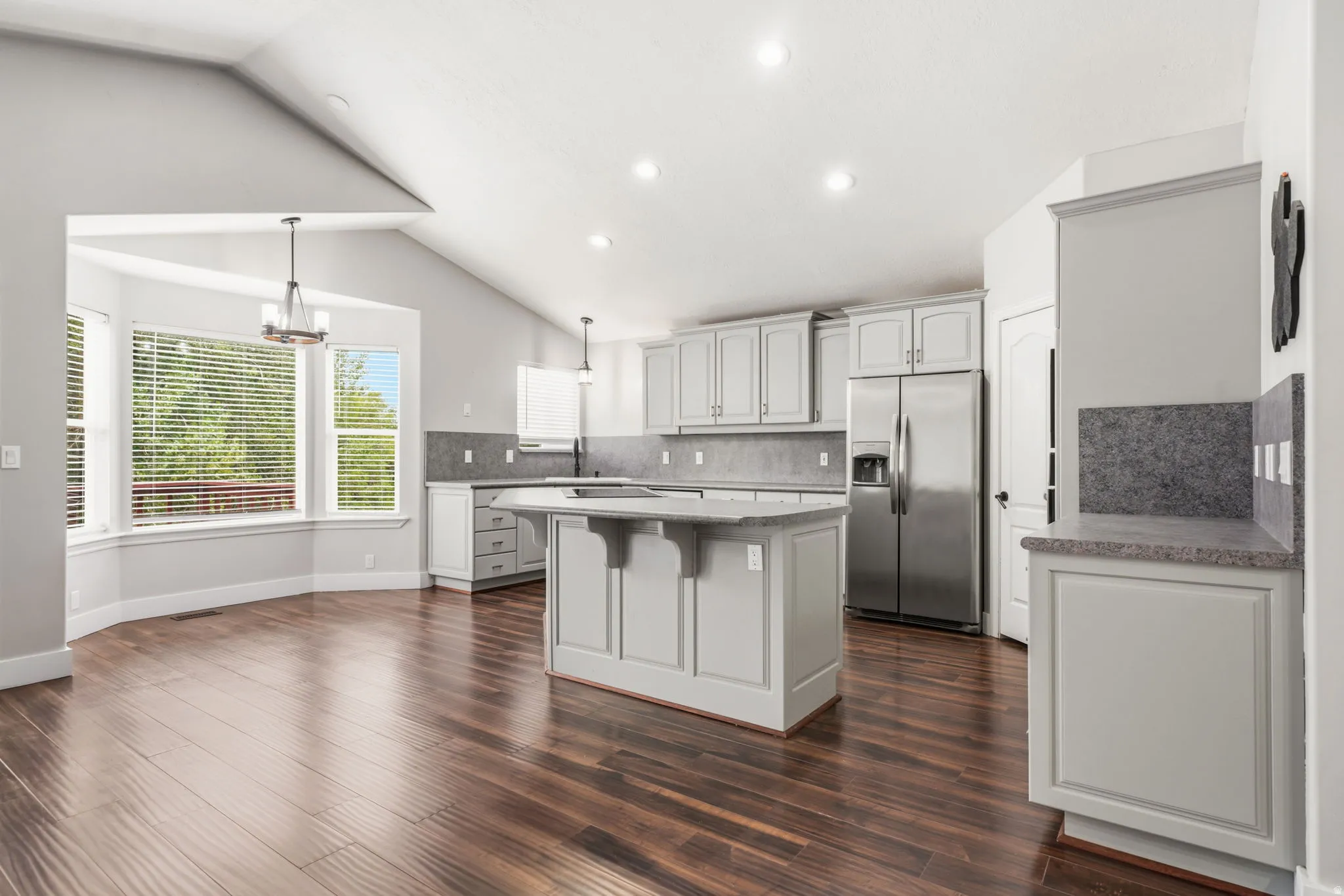 Open-concept kitchen and dining area featuring wood-finish flooring, vaulted ceilings, and recessed lighting