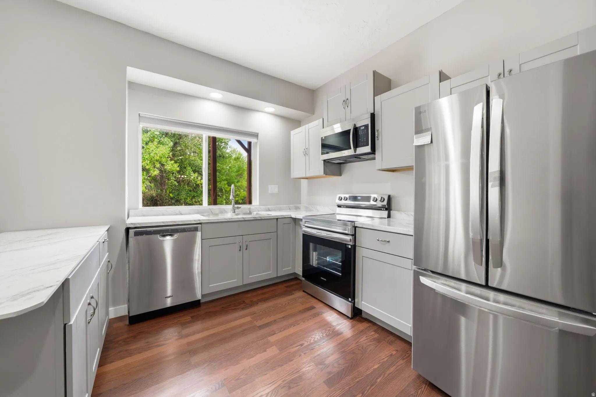 Kitchen featuring light gray cabinetry, stainless steel appliances, marble-look countertops, and wood-finish flooring