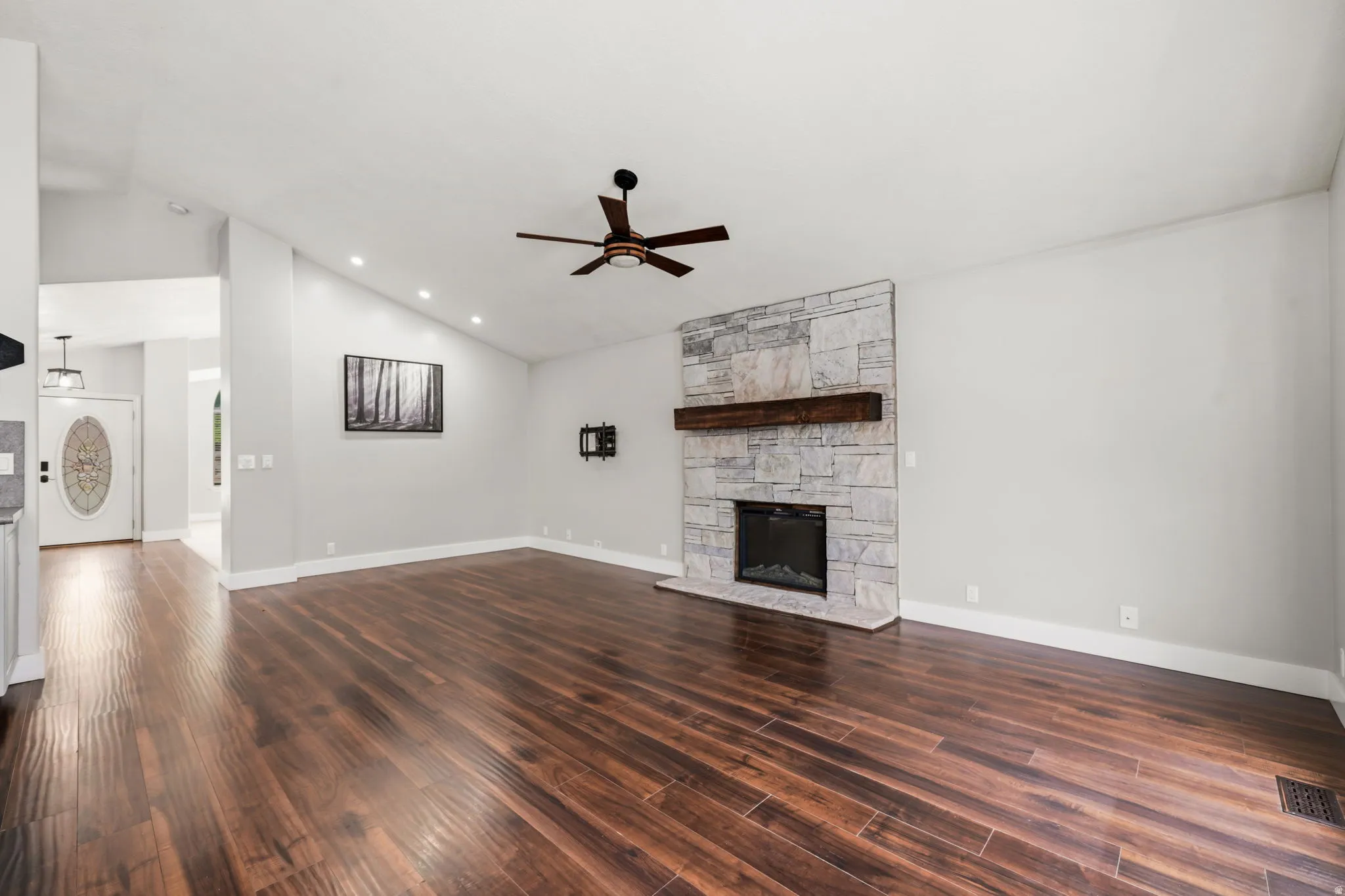 Living area featuring wood-finish flooring, a stone-clad fireplace with a wood mantel, vaulted ceilings, recessed lighting, and a ceiling fan