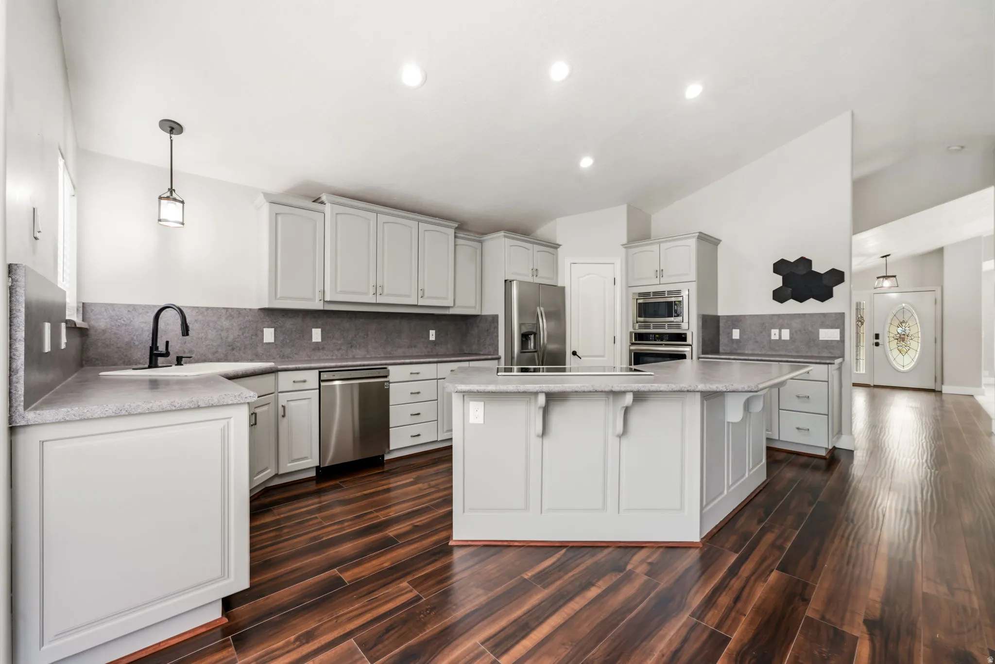 Open-concept kitchen featuring wood-finish flooring, light gray cabinetry, stainless steel appliances, a center island, and recessed lighting