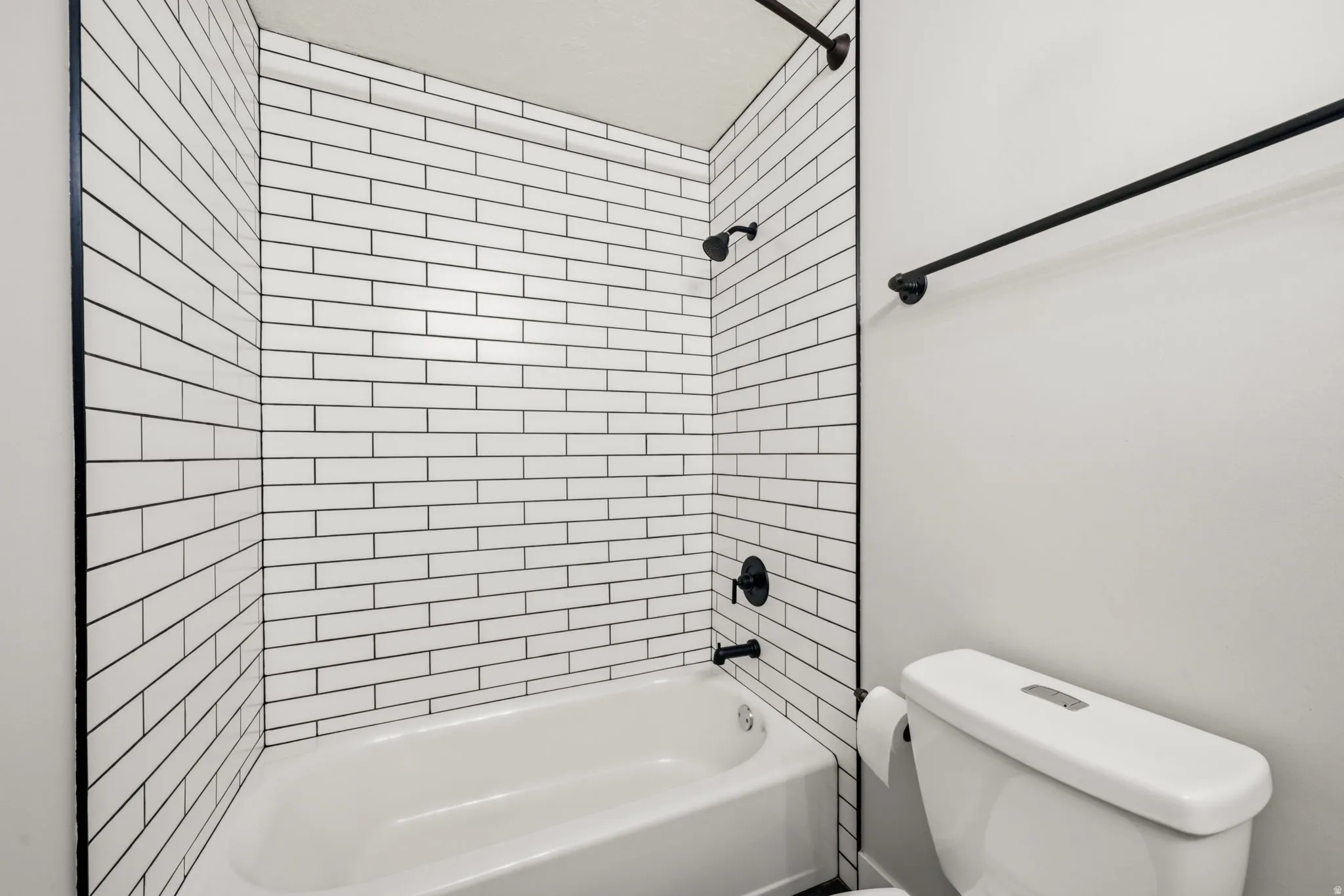 Bathroom featuring a white subway tile surround, matte black fixtures, a white bathtub, and a standard toilet