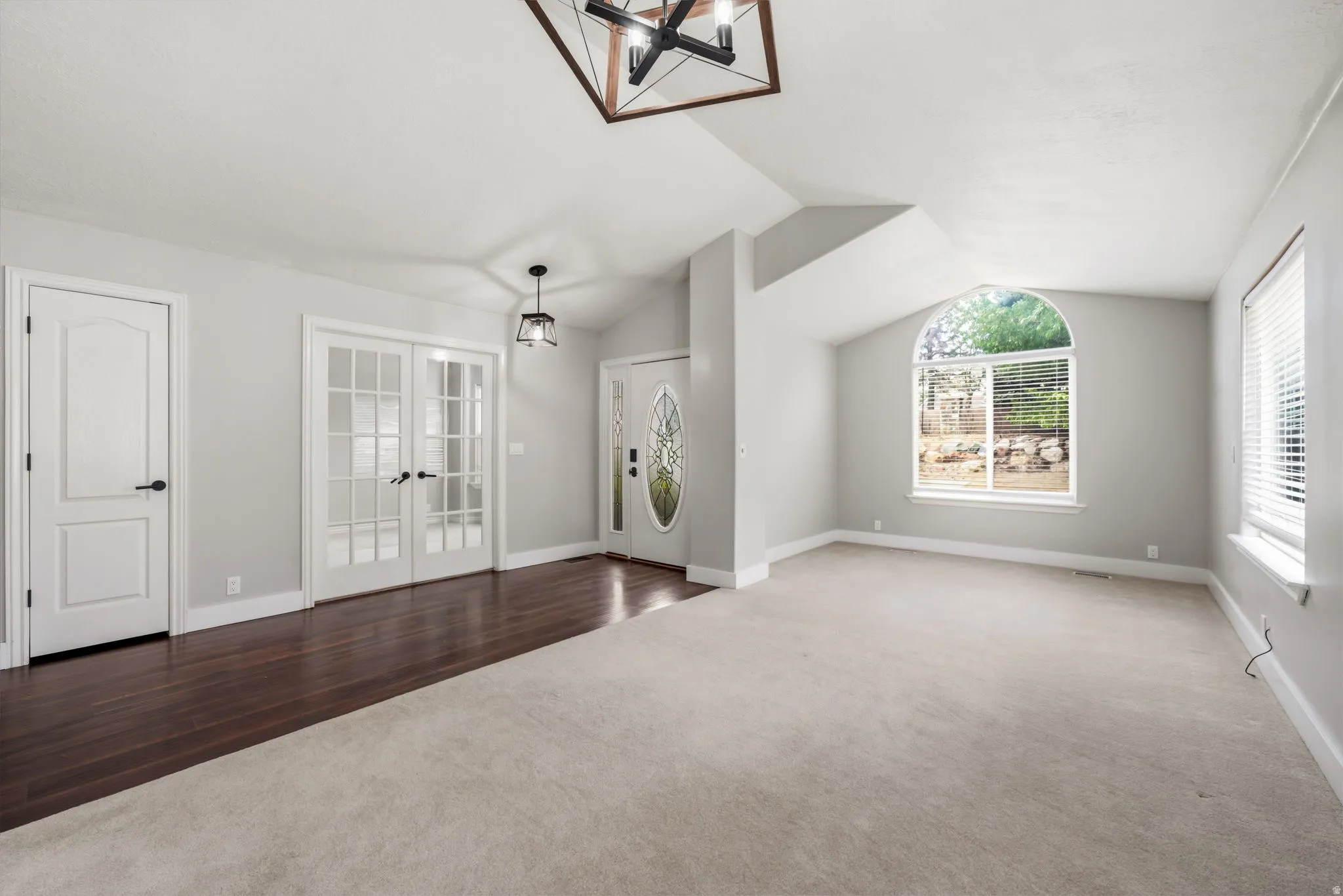 Spacious interior featuring a vaulted ceiling and a mix of light carpeting and dark wood-finish flooring