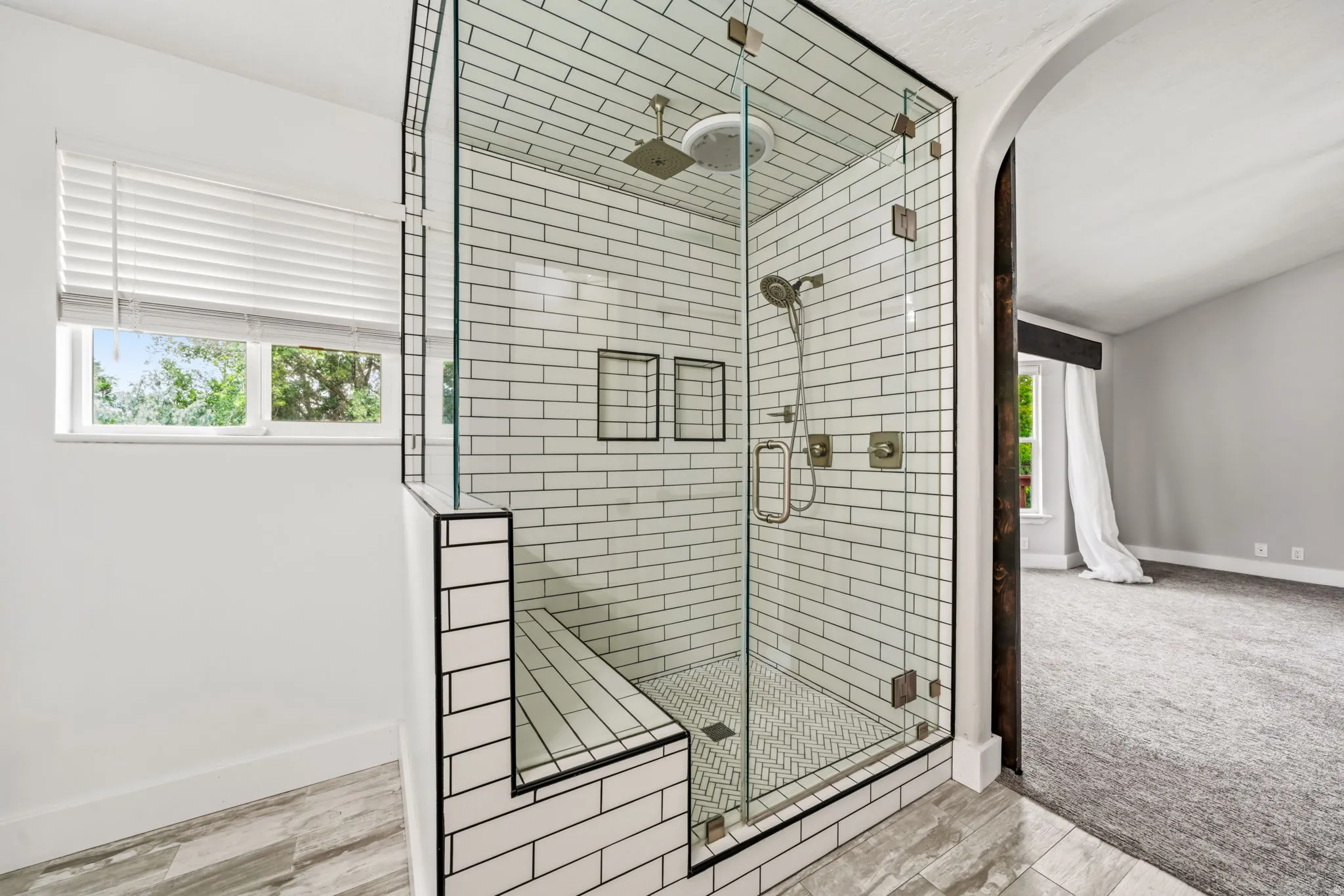 Glass-enclosed shower with subway tile surround, built-in bench, and dual showerheads