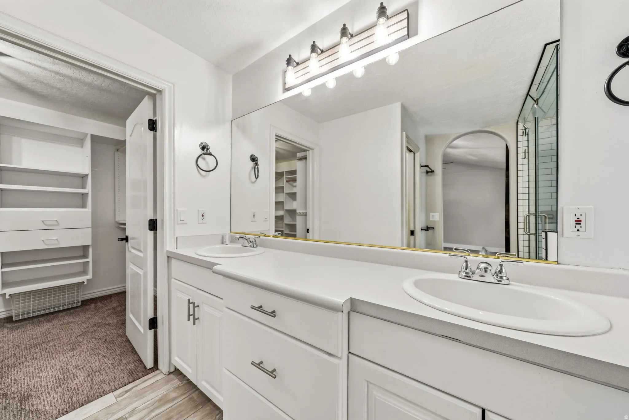 Bathroom featuring dual white sinks with chrome fixtures, a full-width vanity mirror, and white cabinetry with brushed nickel hardware