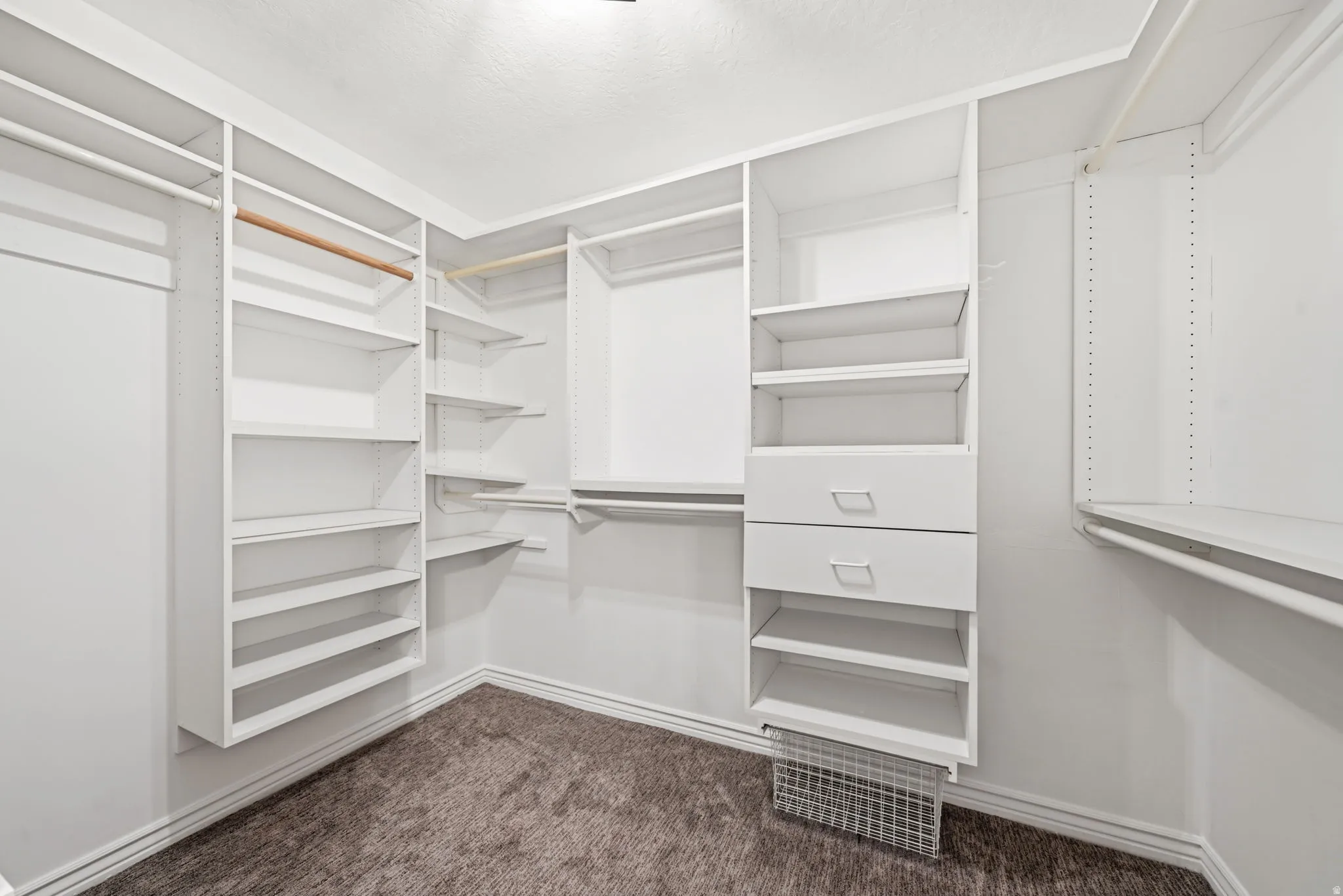 Walk-in closet featuring built-in white shelving, integrated drawers, multiple hanging rods, and dark brown carpeting