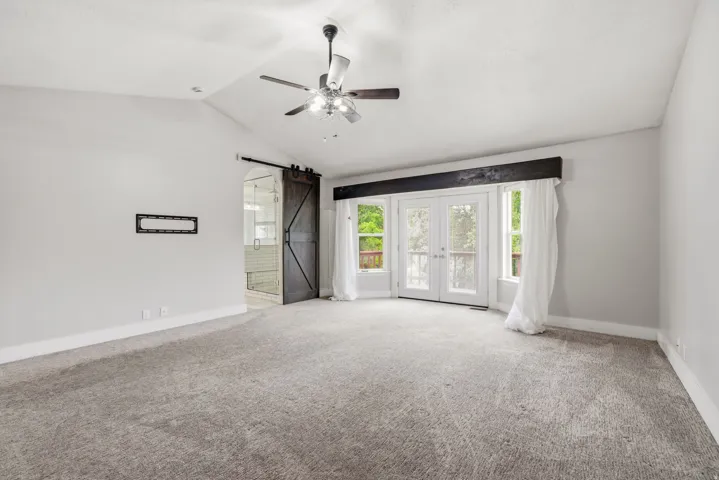Spacious interior featuring a vaulted ceiling with a ceiling fan, plush grey carpeting, and light grey wall finishes