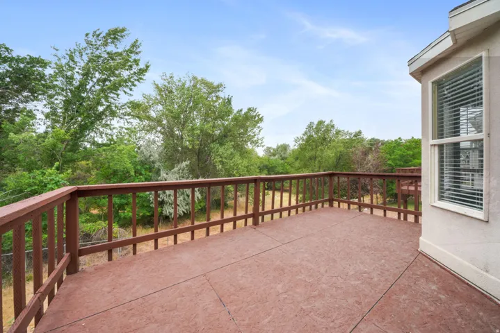 Spacious outdoor deck featuring wood railings, a textured surface, and surrounding mature trees