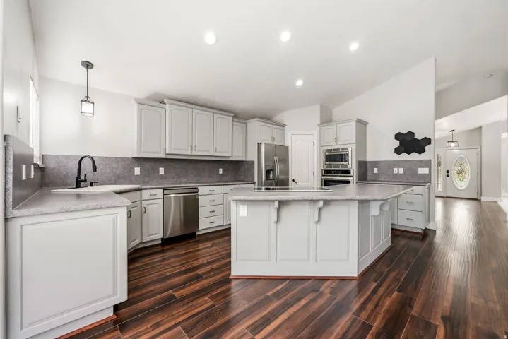 Open-concept kitchen featuring wood-finish flooring, light gray cabinetry, stainless steel appliances, a center island, and recessed lighting