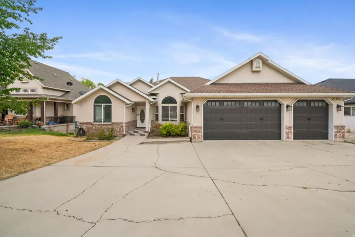 Stucco exterior with stone accents, a multi-car garage, arched window features, a covered entry, and a paved driveway