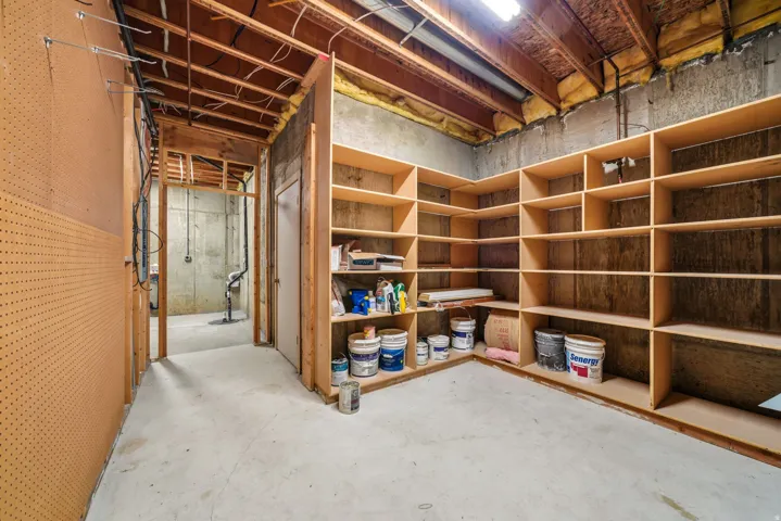 Spacious utility area featuring extensive built-in shelving, durable concrete flooring, exposed ceiling joists, and pegboard wall panels