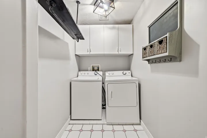 Dedicated laundry area featuring white upper cabinetry, tiled flooring with accenting, and an industrial-style ceiling light fixture