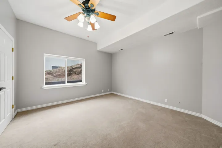 Spacious bedroom showcasing neutral gray walls, plush carpeting, and abundant natural light from a large fixed window