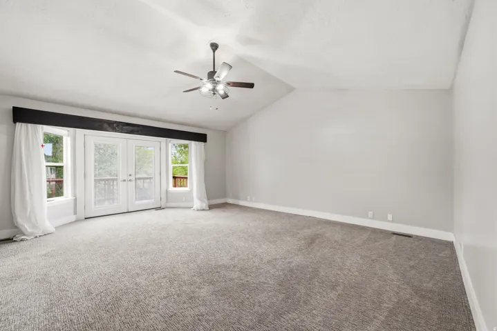 Spacious room featuring vaulted ceilings, a ceiling fan with light fixture, and textured gray carpeting