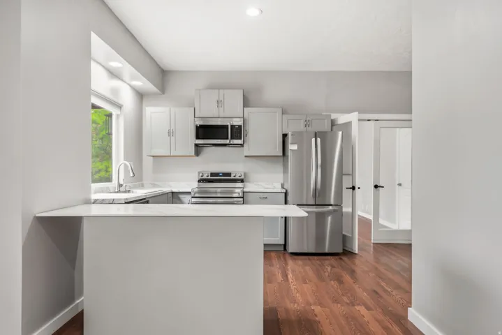 Modern kitchen featuring stainless steel appliances, light gray cabinetry, white countertops, and wood-finish flooring