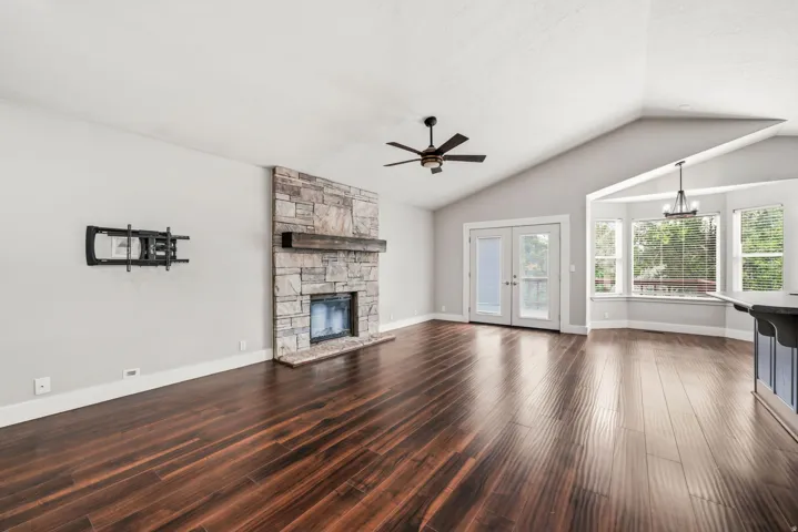 Spacious living area featuring wood-finish flooring, a stacked stone fireplace with a substantial wood mantel, and vaulted ceilings