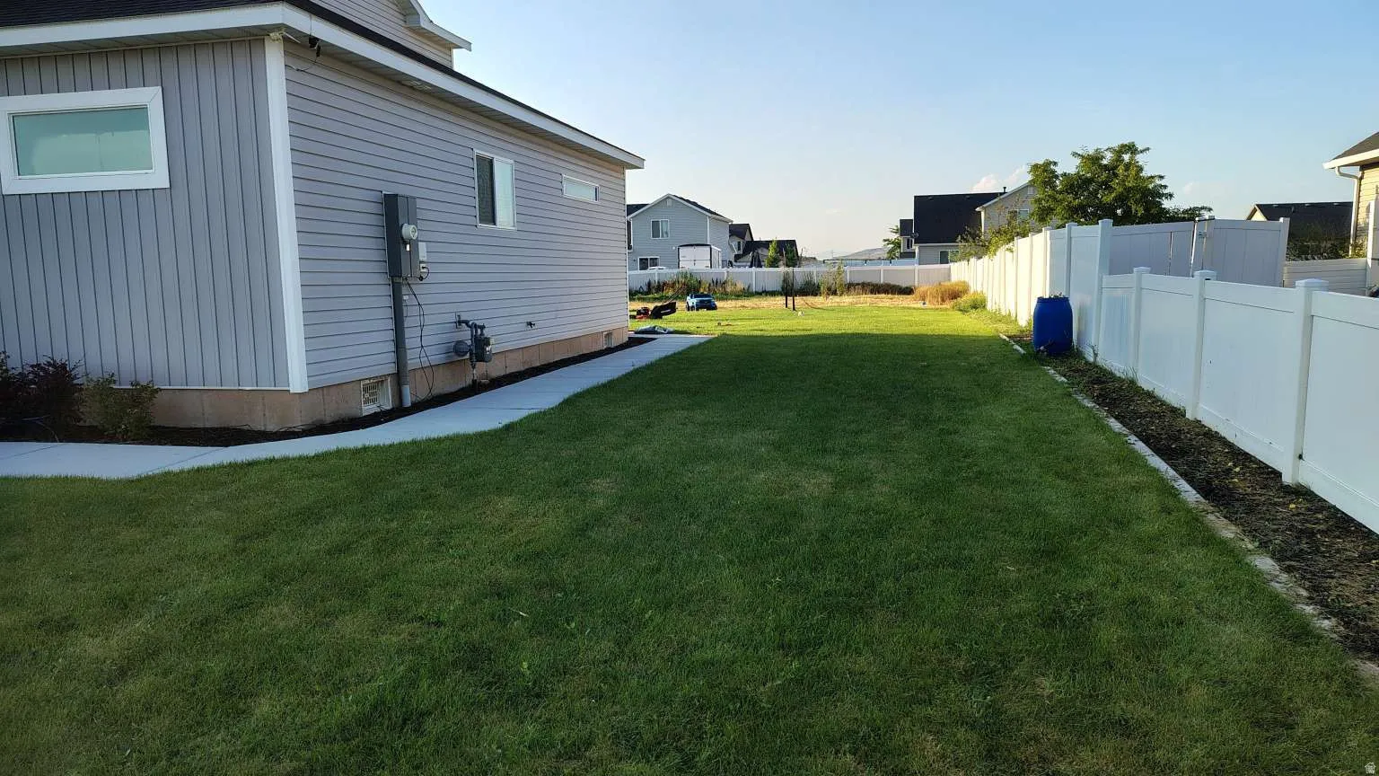 Expansive grassy yard area with a white privacy fence and a concrete walkway