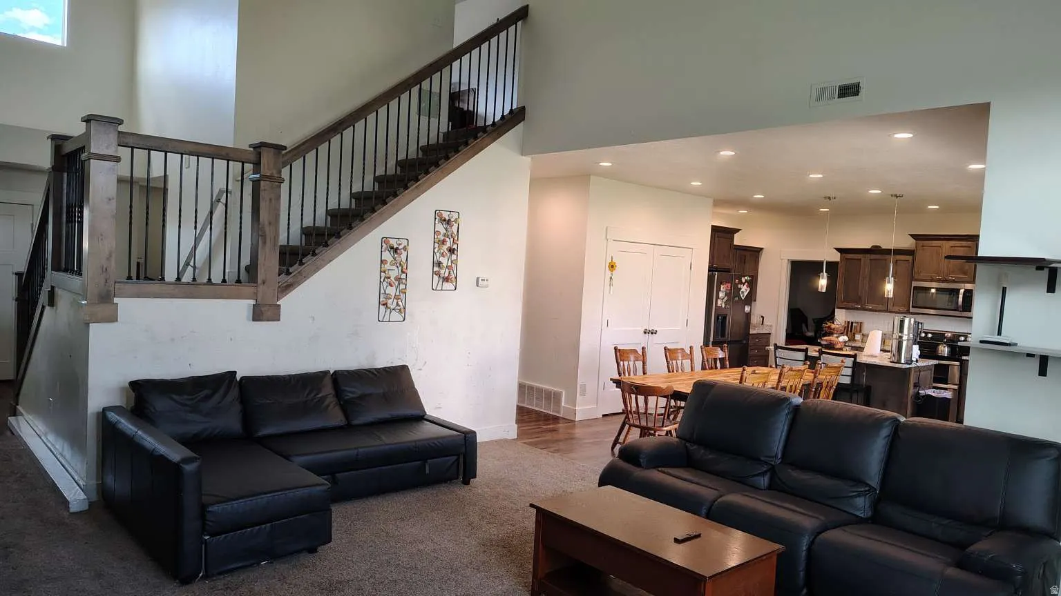 Two-story ceiling, open-concept design, wood-finish flooring, recessed lighting, and a prominent staircase with dark wood and black metal railings