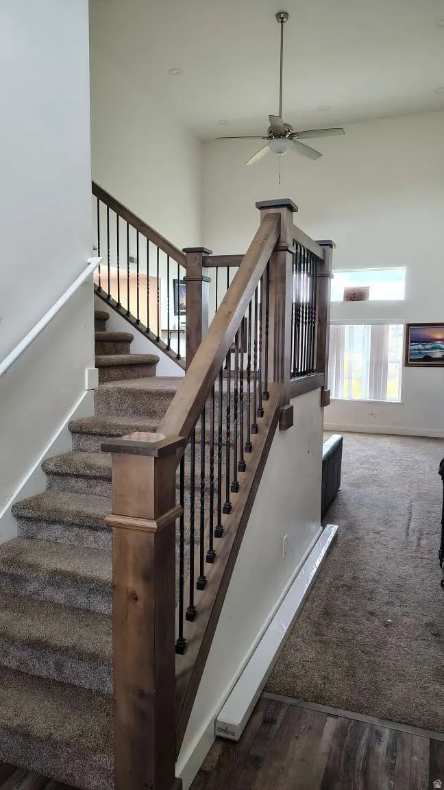 Open-concept living area with soaring ceilings, a ceiling fan, and a staircase featuring wood newel posts and metal balusters