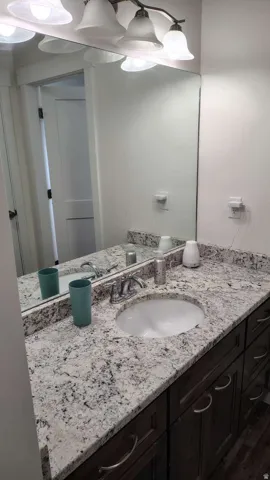 Vanity with an integrated oval sink, stone-finish countertop, dark wood-finish cabinetry, and a chrome faucet