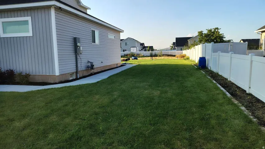 Expansive grassy yard area with a white privacy fence and a concrete walkway