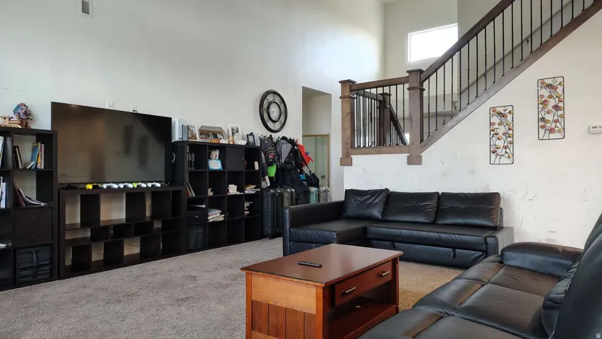 Carpeted living area with high ceilings, upper wall window, and a staircase featuring wood-finish handrails and black metal balusters