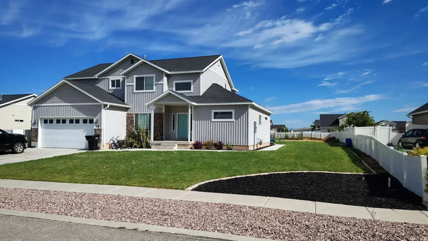 Two-story residence featuring gray siding and stone accents, a two-car garage, and a covered entry