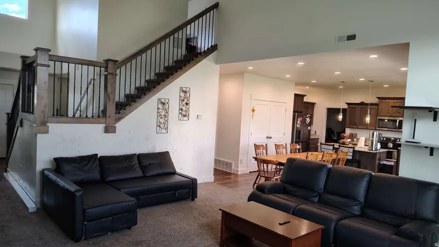 Two-story ceiling, open-concept design, wood-finish flooring, recessed lighting, and a prominent staircase with dark wood and black metal railings