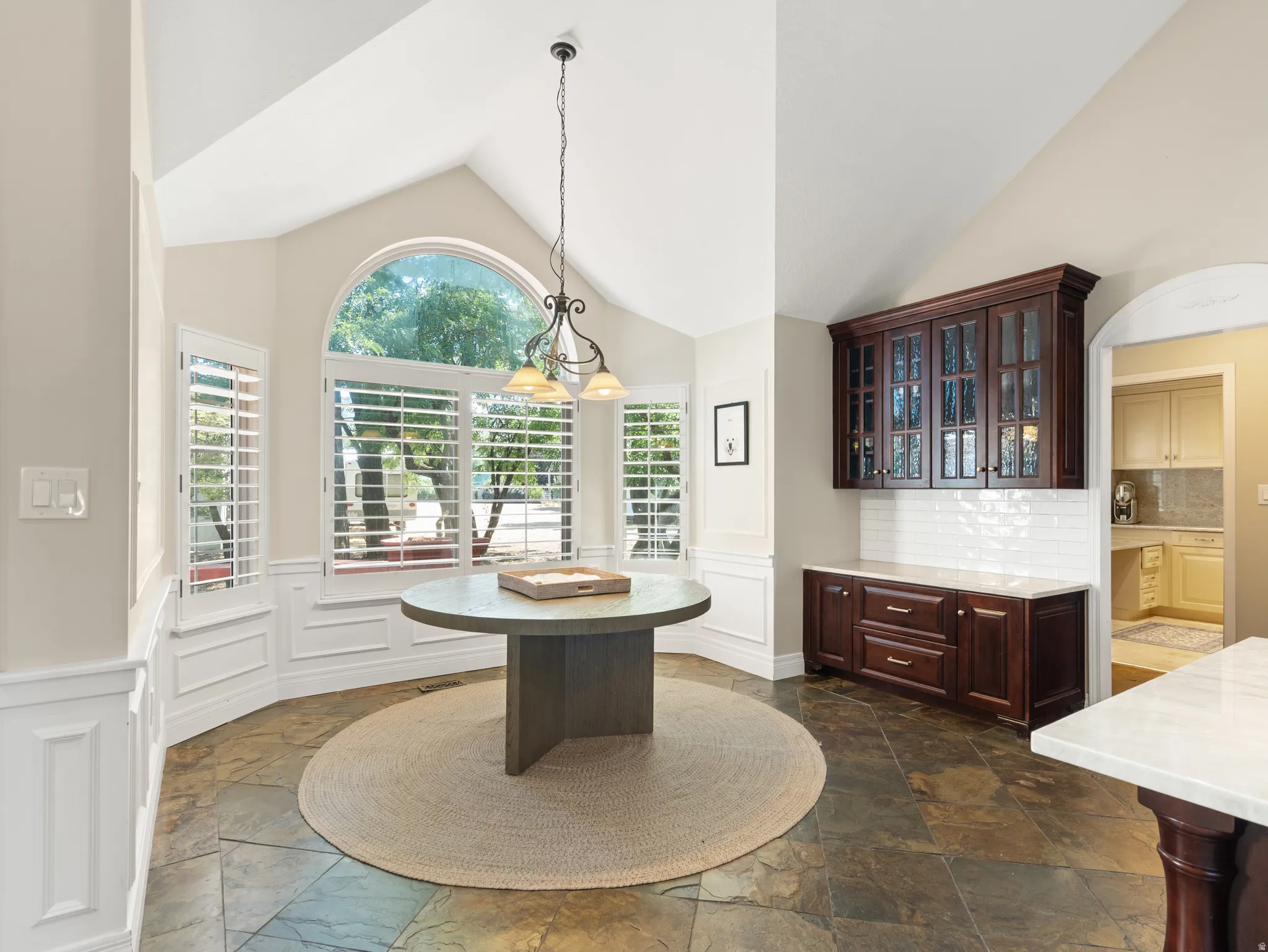 Vaulted ceiling with an arched window, plantation shutters, and multi-tone tile flooring