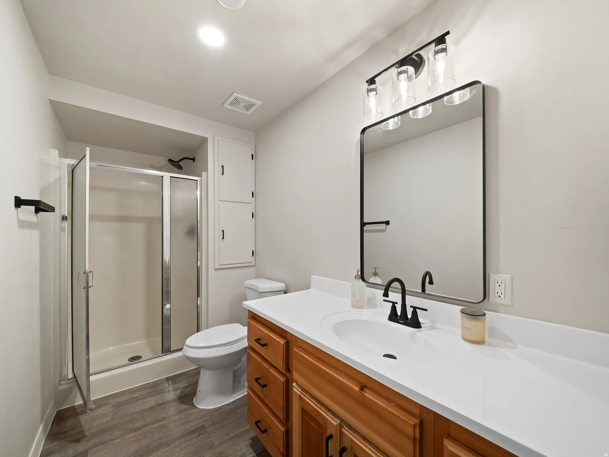 Bathroom featuring a wood-finish vanity with a white countertop, an undermount sink, and matte black fixtures