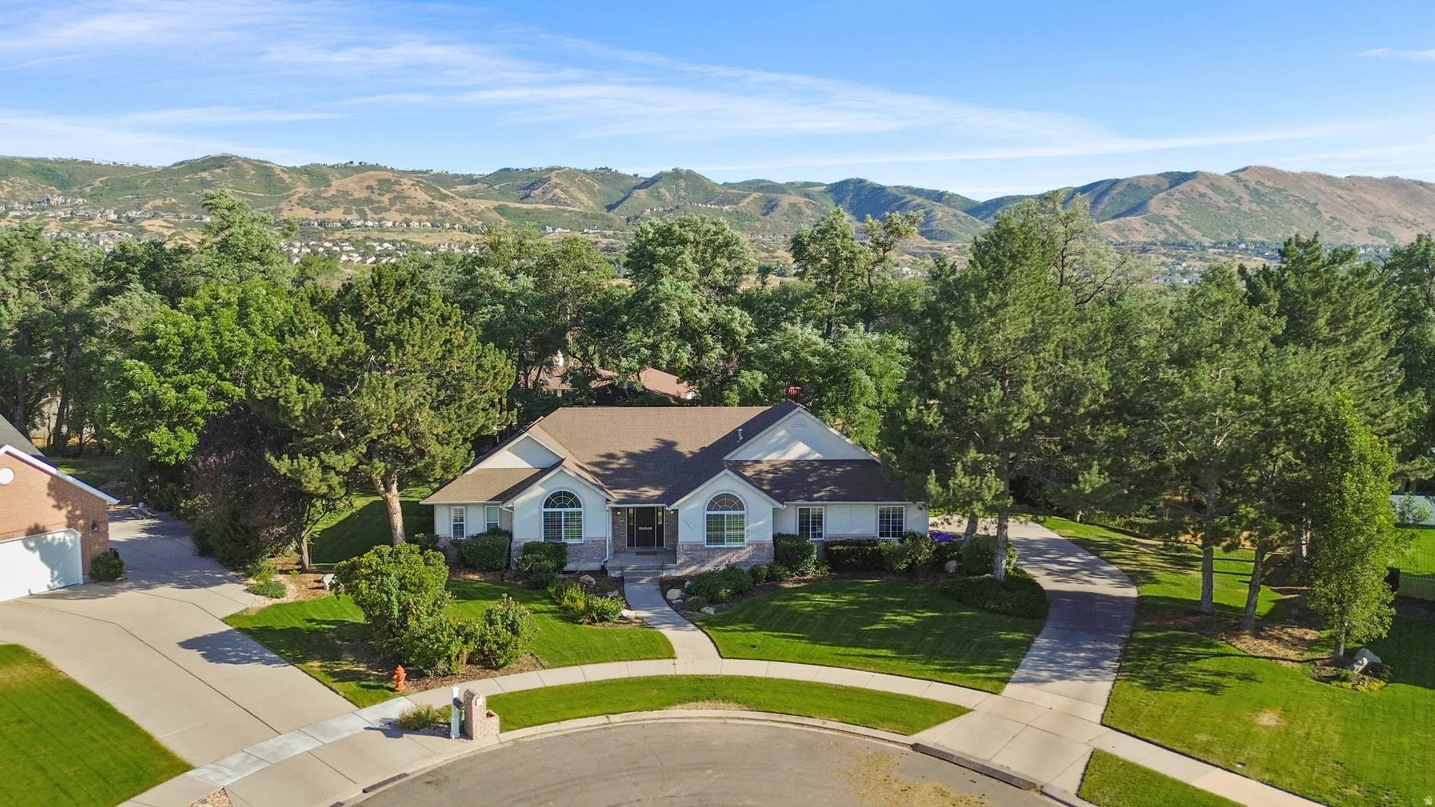 Expansive property with a white exterior, brown shingle roof, and a mature tree canopy