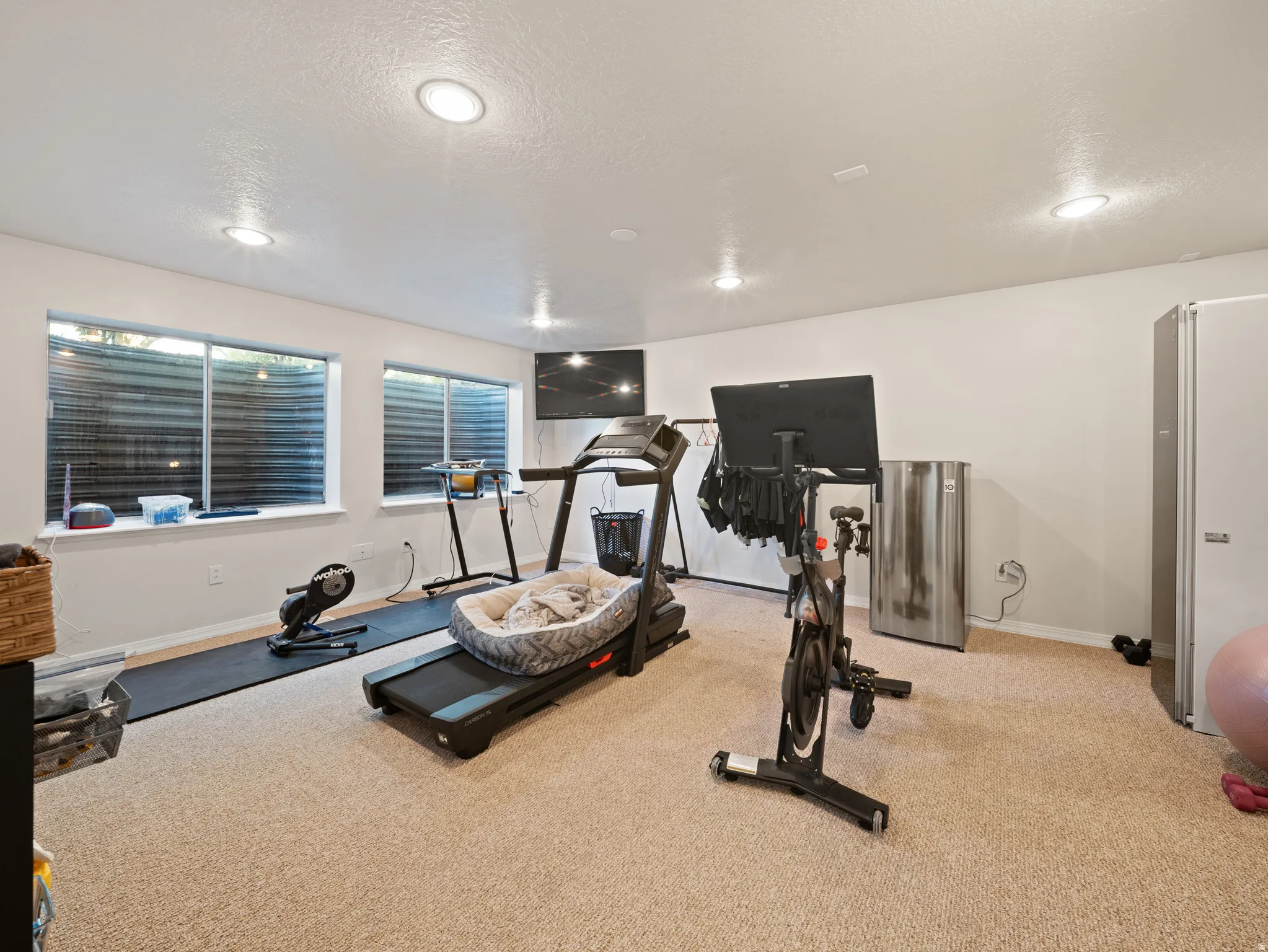 Finished basement space featuring recessed lighting, a neutral carpet, two egress windows with horizontal blinds, and painted white walls