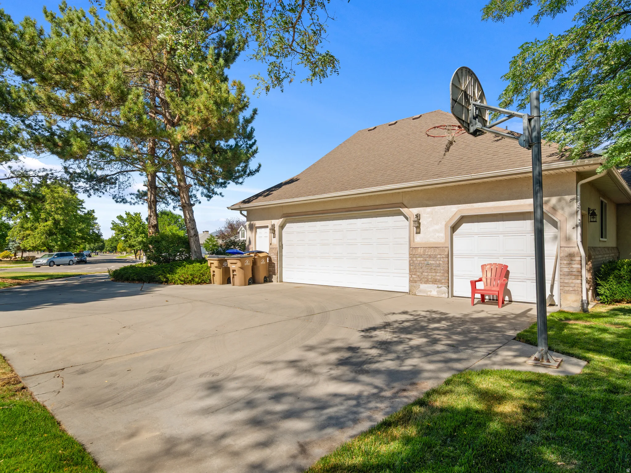 Three-car garage with two white roll-up doors and one single white roll-up door, featuring a brick facade accent