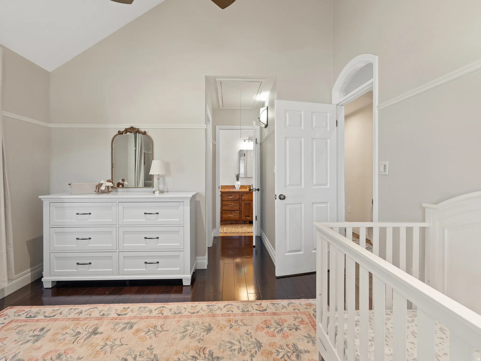 Vaulted ceiling room with wood-finish flooring, featuring an arched doorway and a hallway beyond