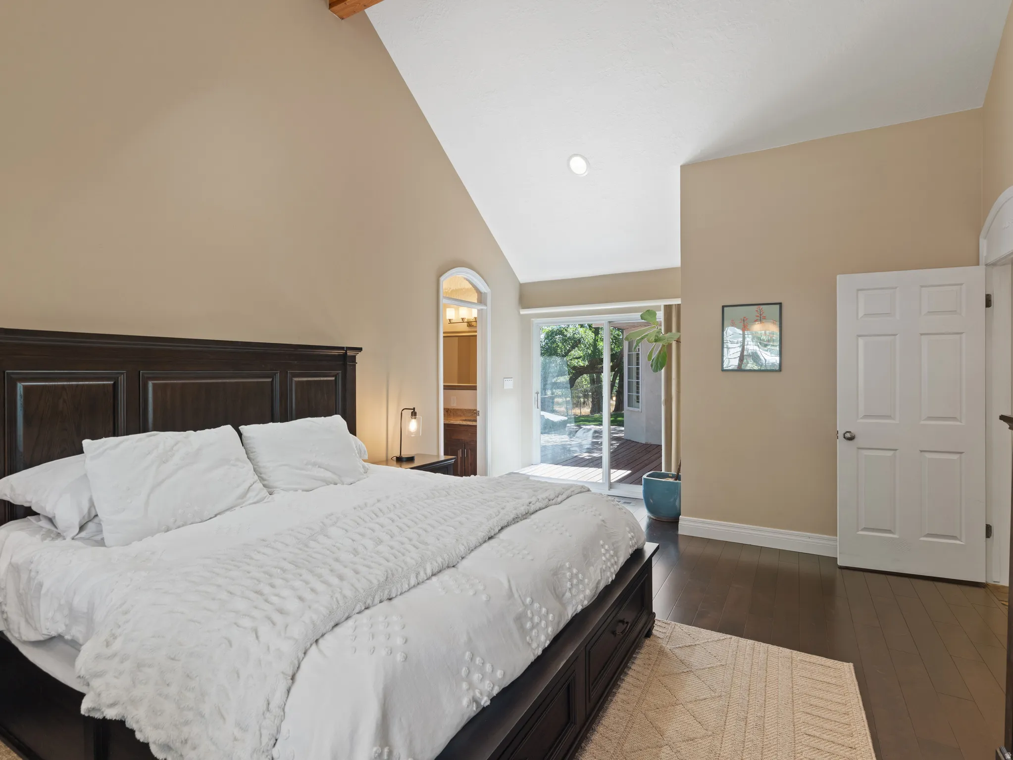Vaulted ceiling with exposed wood beam, dark wood-finish flooring, sliding glass door access to a patio, and an arched entry