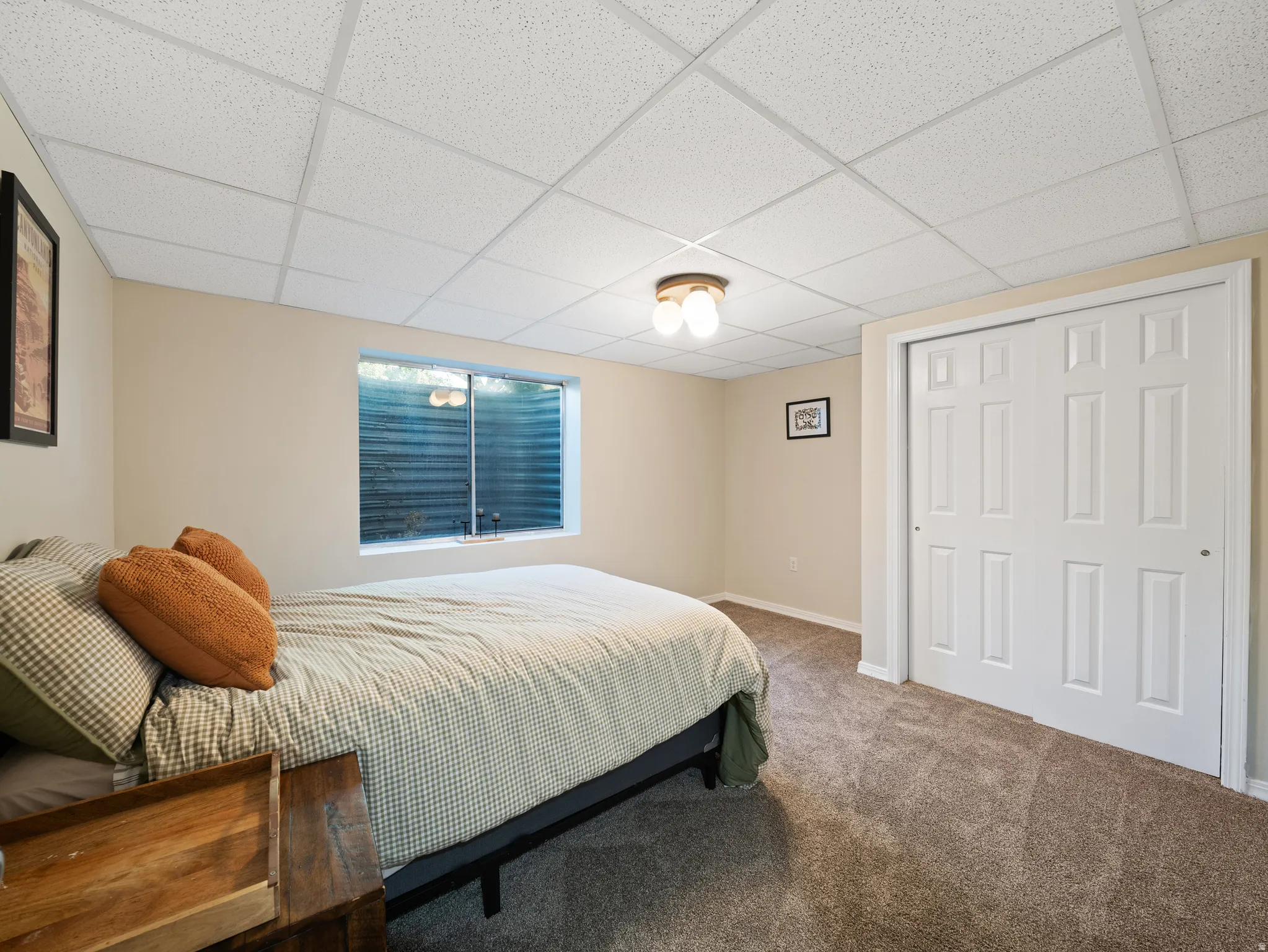 Carpeted room featuring a drop ceiling, a horizontal window with blinds, and white bi-fold closet doors