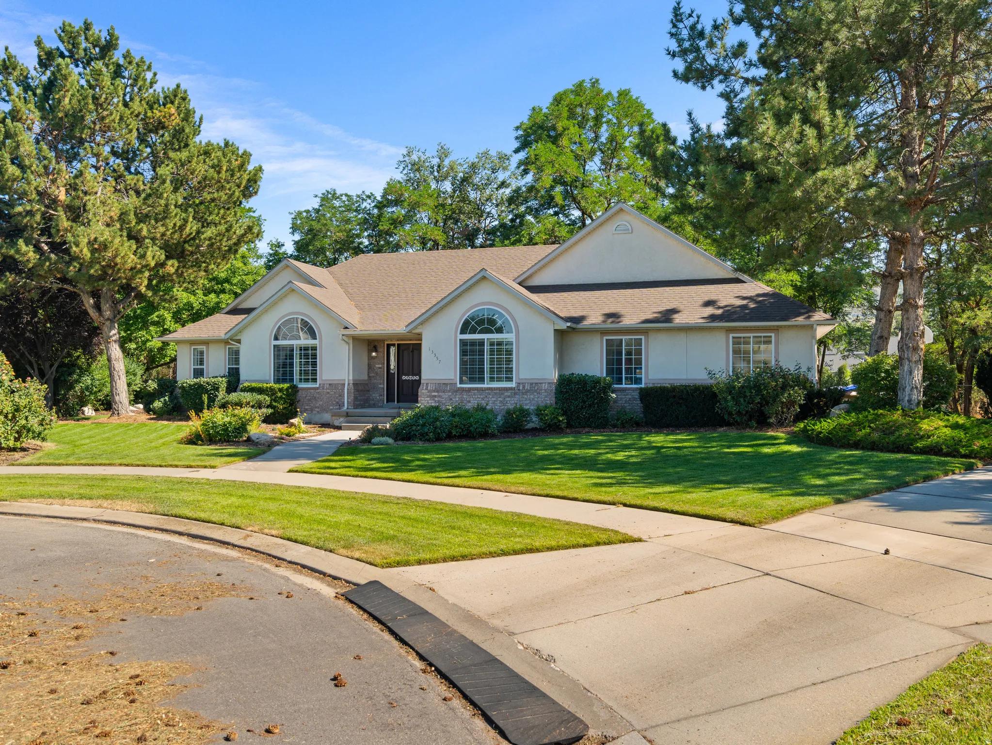 Stucco and stone exterior featuring arched windows, a covered entry, and a multi-car concrete driveway