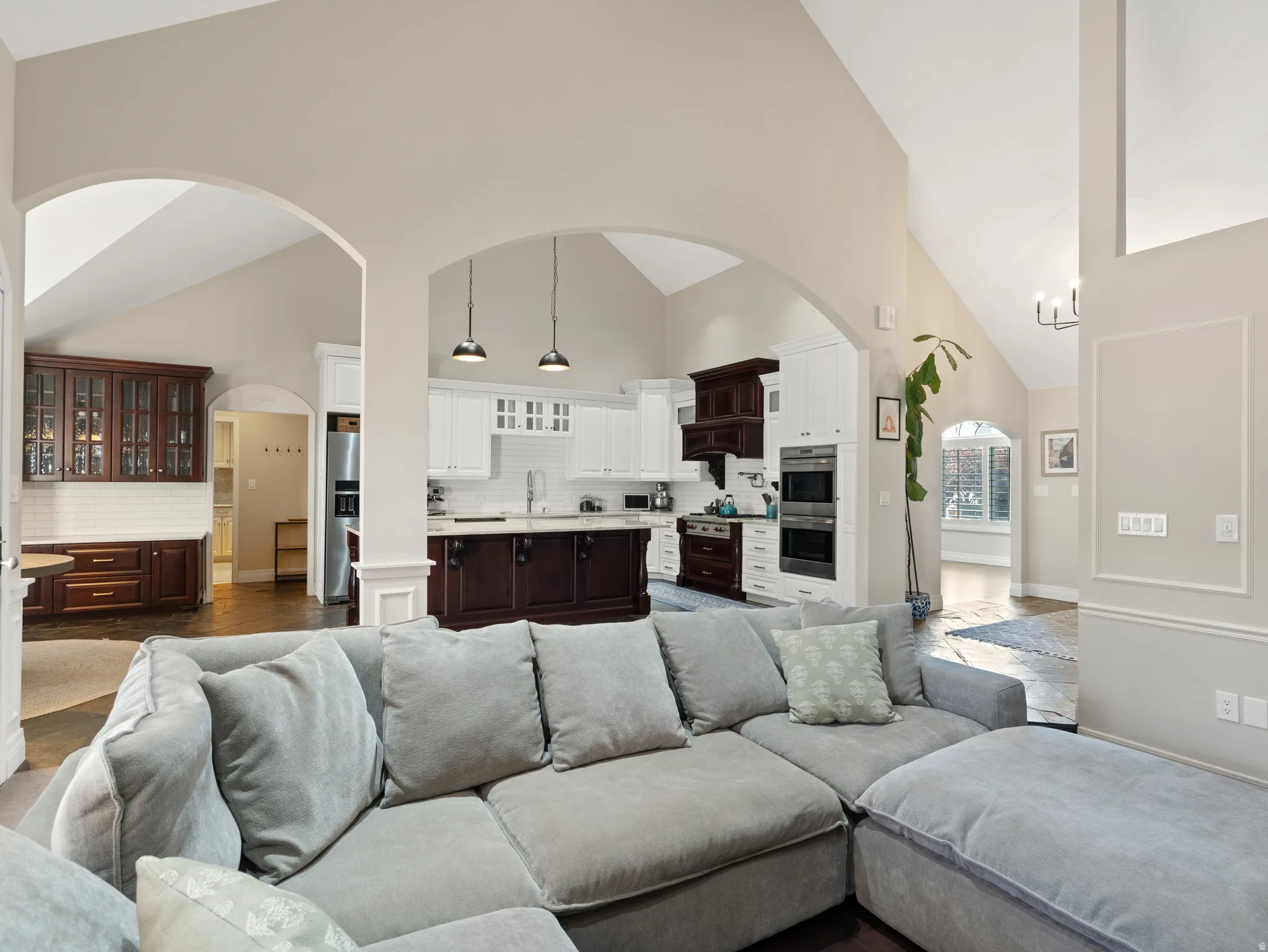 Open concept living space featuring vaulted ceilings, arched doorways, a gourmet kitchen with an island, and a separate built-in bar area with glass-front cabinetry
