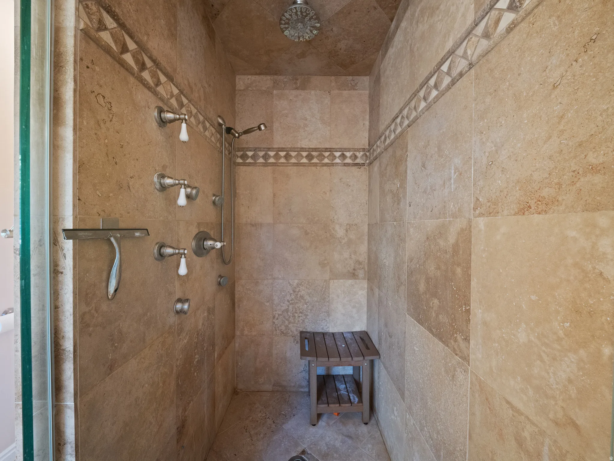 Tiled shower stall featuring multiple shower heads, a handheld shower fixture, and decorative accent tiling