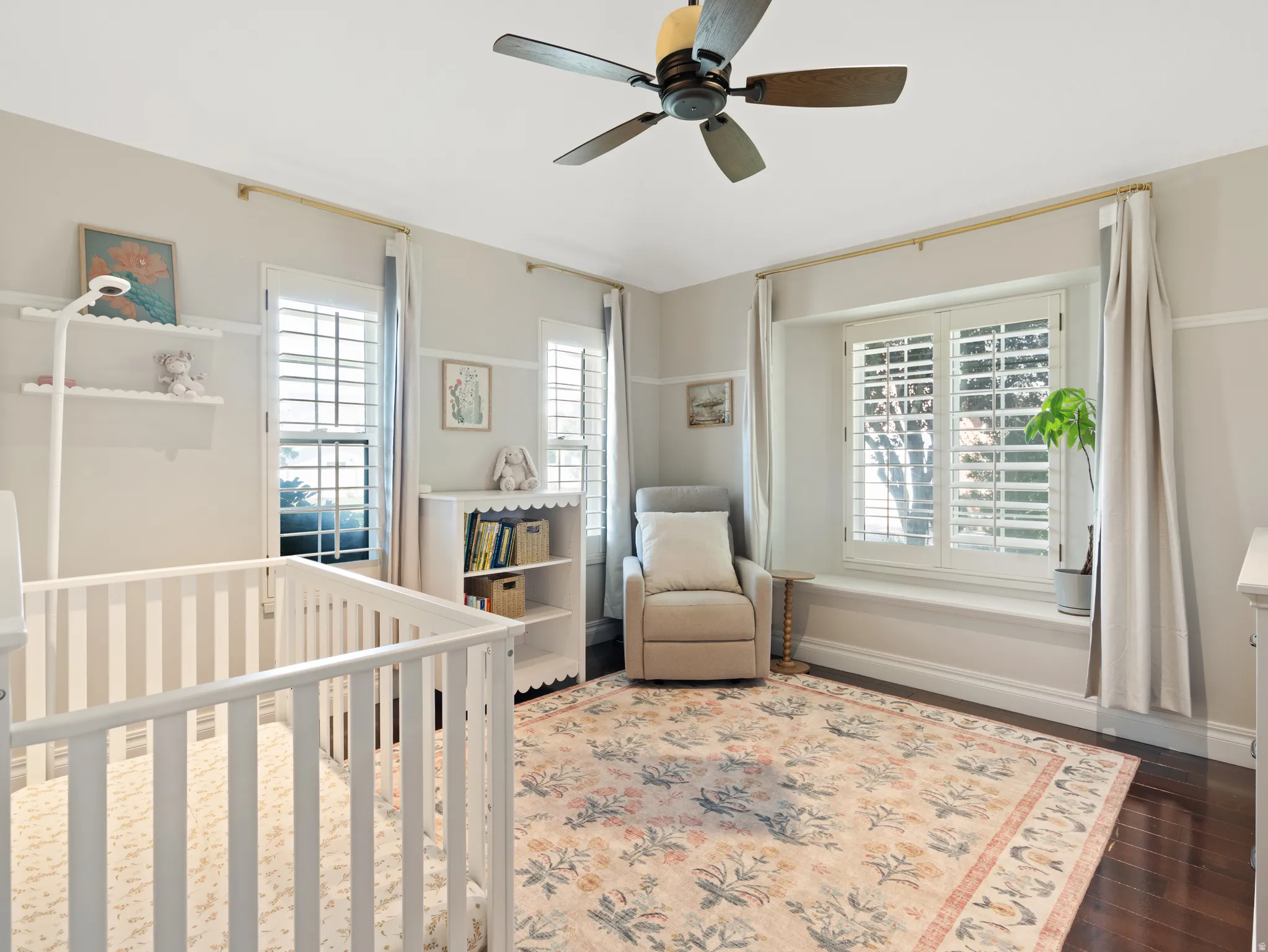 Well-appointed room featuring dark wood-finish flooring, a ceiling fan, and multiple windows with plantation shutters