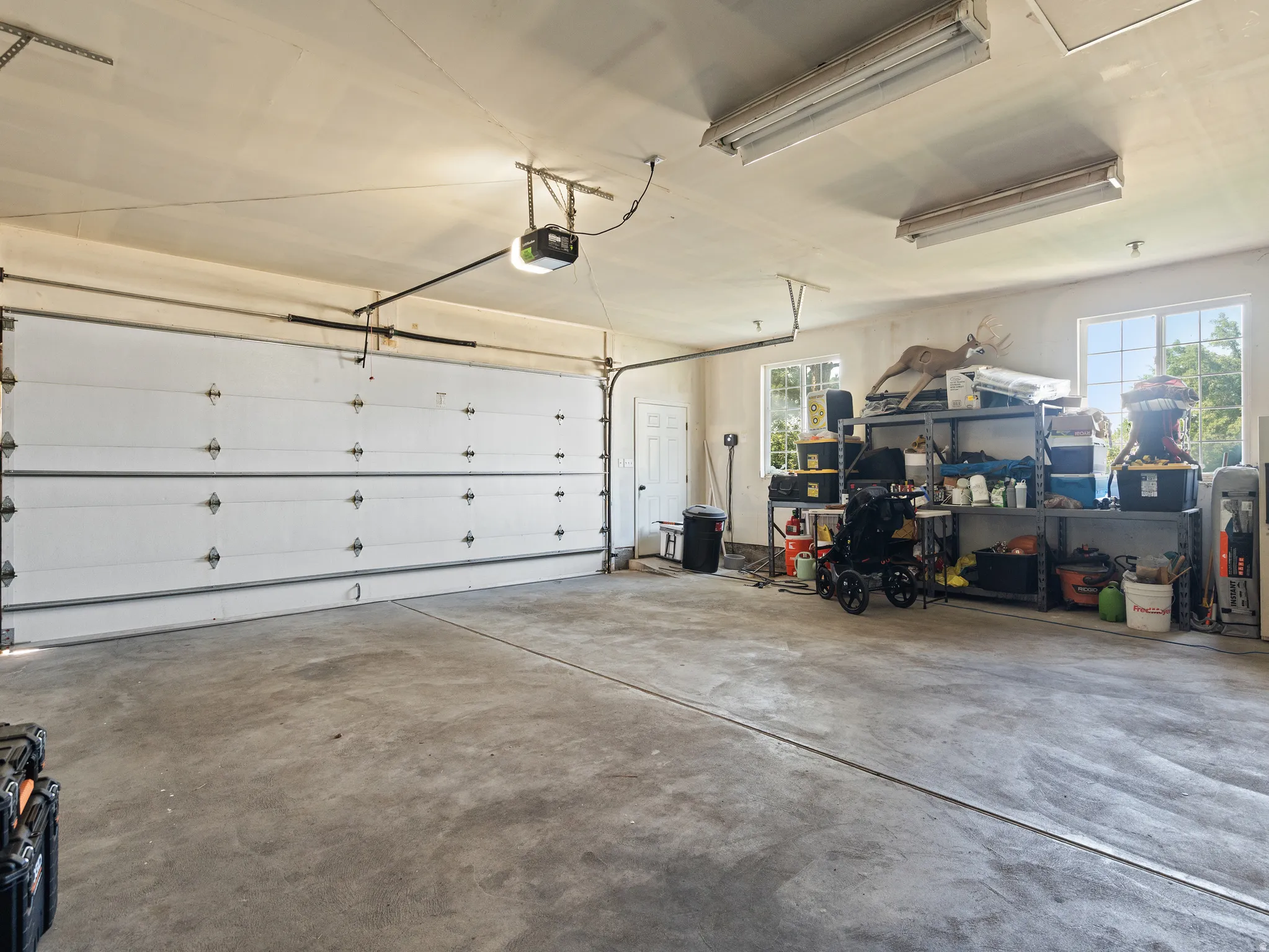 Spacious garage featuring a concrete floor, overhead fluorescent lighting, two windows, and a side entry door