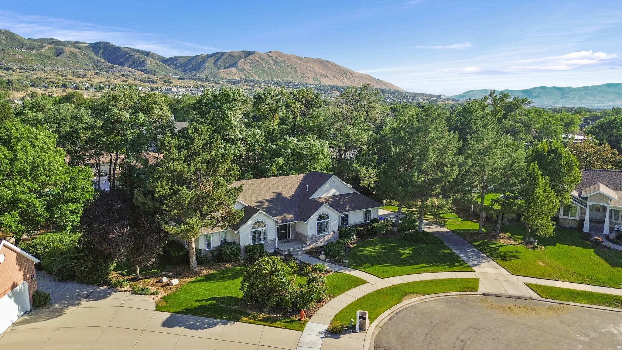 Sizable residential property featuring a light-colored exterior, an expansive green lawn, and mature trees